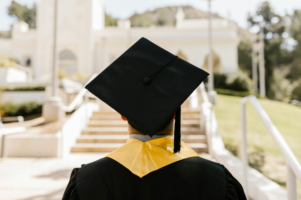 DAAD Scholarship for students worldwide 2025 Back view of a graduate in a cap and gown standing outdoors facing a building.